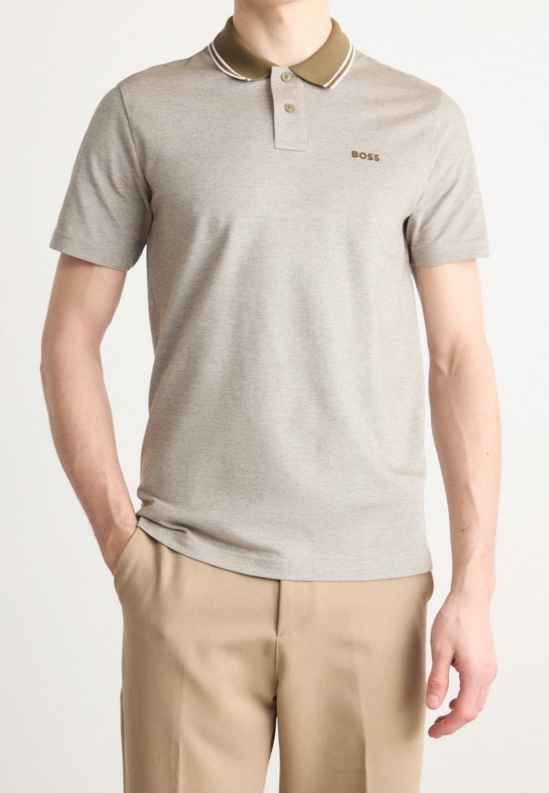 Polo de couleur gris clair avec un col kaki et deux rayures blanches. Dispose d'une patte de boutonnage à l'avant, de manches courtes et d'un logo de marque discret.