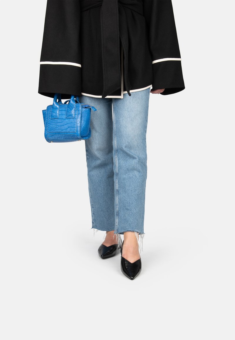 Zwarte jas met witte bies, lichtblauwe jeans met slijtageplekken, zwarte schoenen met een puntige neus en een kleine blauwe handtas met structuur.