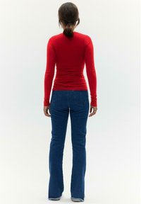 Rode langemouwen top gecombineerd met blauwe flared jeans. De top heeft een aangesloten ontwerp, terwijl de jeans aan de zoom een lichte slijtage vertonen.