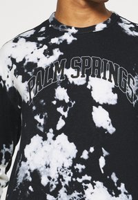 Sudadera de manga larga negra con un patrón de teñido anudado en blanco y gris, con "PALM SPRINGS" impreso en letras negras en negrita en el pecho.