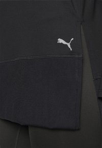 Czarny sportowy top z prążkowanym wykończeniem, z małym białym logo Puma z boku. Gładka faktura i dopasowany krój.