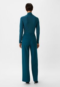 Türkises Langarmoberteil mit hohem Kragen, kombiniert mit weiten türkisfarbenen Hosen, die elegante Linien und eine glatte Textur aufweisen.