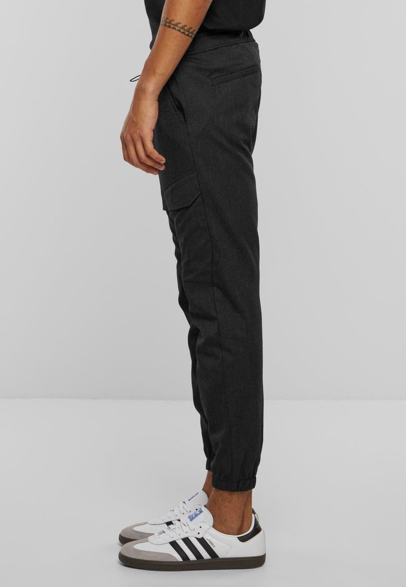 Dark gray jogger pants with elastic cuffs, side cargo pockets, and a smooth textured fabric, paired with white sneakers with black stripes.