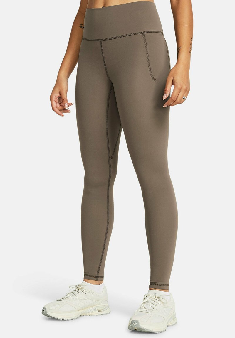 Högmidjade bruna leggings gjorda av stretchigt material, med plattlockade sömmar och en sidficka för bekvämlighet. Kombineras med vita sneakers.