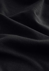 Tessuto nero con una texture liscia e opaca, che mostra morbide pieghe e sottili variazioni di luce, evidenziando il suo colore uniforme e la morbidezza.