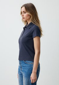 Polo navy con colletto, maniche corte e chiusura a due bottoni. Abbinato a jeans blu scoloriti. Texture del tessuto liscia.