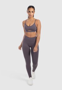 Un reggiseno sportivo e leggings a vita alta in tessuto grigio scuro, con un design a taglio sul reggiseno e una texture liscia e elasticizzata.