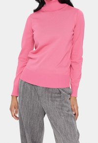 Tajta rosa turtlenecktröja med ribbad struktur; kombinerad med grå randiga löst sittande byxor. Enkelt och modernt design.