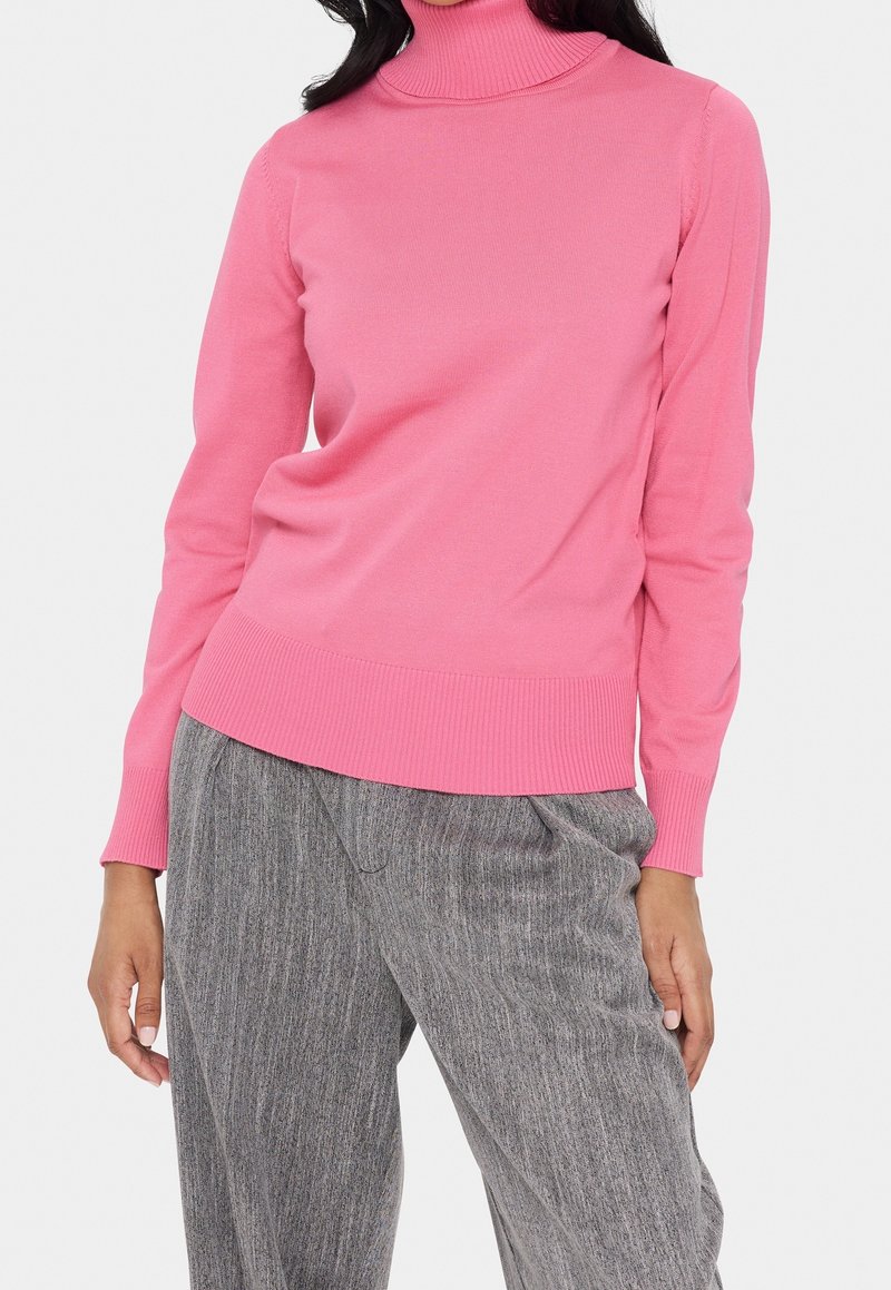 Tajta rosa turtlenecktröja med ribbad struktur; kombinerad med grå randiga löst sittande byxor. Enkelt och modernt design.