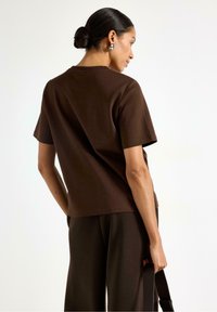 T-shirt in cotone marrone con maniche corte e vestibilità comoda. Tessuto liscio, design a girocollo e dettagli di cucitura sottili visibili.