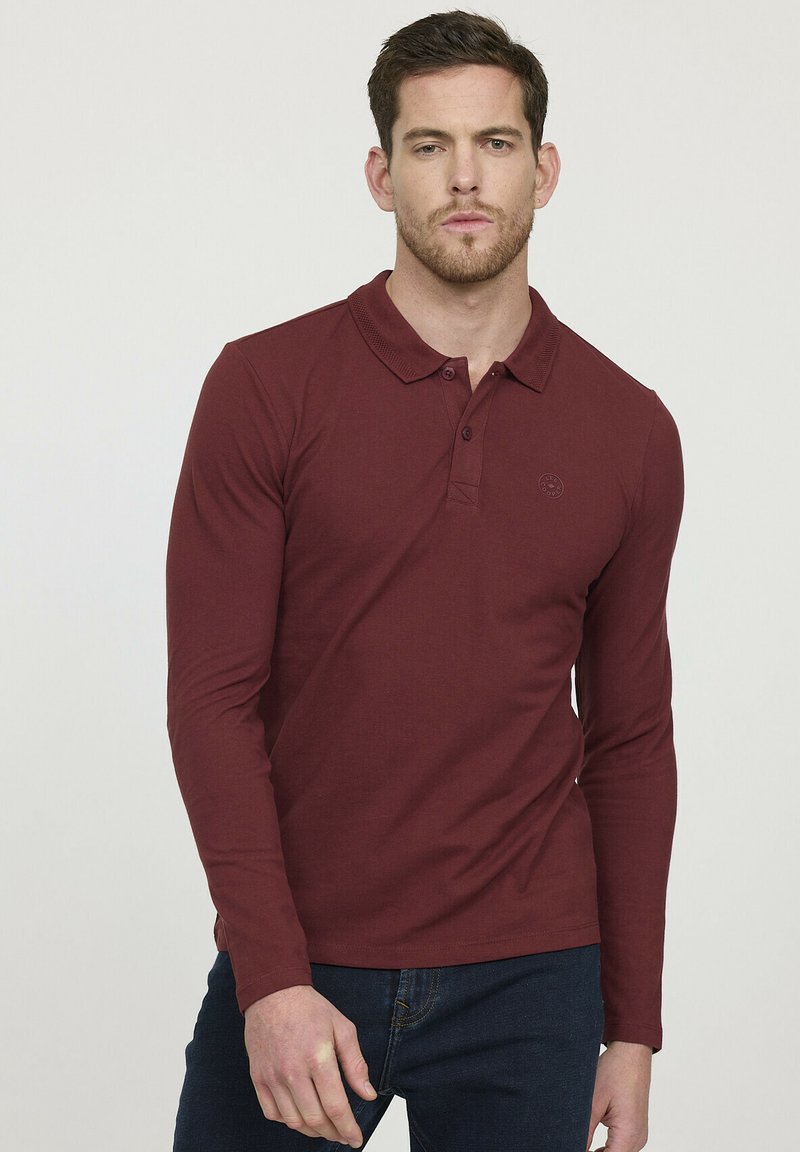 Polo shirt bordeaux à manches longues avec un col, une fermeture à trois boutons et un logo subtil sur la poitrine gauche. Texture en coton lisse.