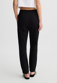 Pantaloni neri a sigaretta con una vestibilità comoda, vita elastica e risvolti. Tessuto liscio con una consistenza morbida, senza pattern visibili o accessori metallici.
