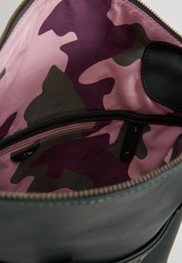 Otwarte czarne skórzane torba, ukazująca różową, fioletową i szaro-kamuflażową podszewkę z wewnętrzną kieszenią na zamek.