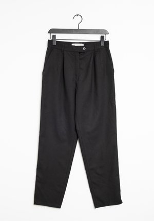 Zwarte high-waist taps toelopende broek met riemlussen en zijzakken, hangend aan een zwarte plastic hanger tegen een witte achtergrond.