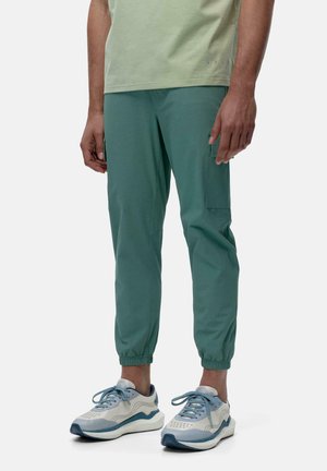 Green tapered athletic pants with cargo pockets, elastic cuffs, and a smooth texture, paired with light blue sneakers featuring mesh and rubber accents.