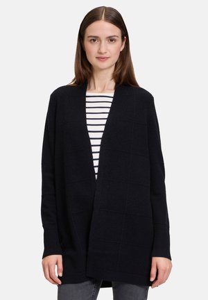 Black cardigan with open front, textured pattern, ribbed cuffs, and long sleeves, layered over a striped shirt. Straight fit and soft fabric.