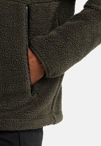 Flauschige olivgrüne Reißverschluss-Fleecejacke mit strukturierter Oberfläche, ausgestattet mit einer Seitentasche und gerippten Bündchen für zusätzlichen Komfort.