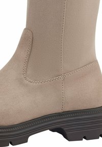 Beżowy botek do kostki wykonany z miękkiej, teksturowanej tkaniny o gładkim wykończeniu, z kontrastującą ciemną podeszwą i widocznymi detalami szycia.