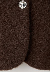 Tessuto marrone con una texture soffice, caratterizzato da un bottone argentato lucido come dettaglio principale.