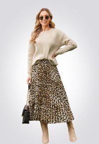 Pull en tricot beige associé à une jupe maxi plissée à imprimé léopard. Les accessoires comprennent un sac à main noir et des bottes marron montant jusqu'aux genoux.