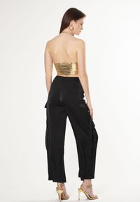 Gouden metallic strapless top gecombineerd met zwarte cargo broeken. Extra details zijn zijzakken en hoge gouden sandalen.