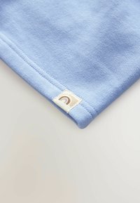 Blå bomuldsstof med en glat tekstur, prydet med et mærke med et brunt regnbue-design i kanten. Blødt og afslappet look.
