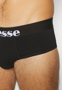 Schwarze Baumwoll-Boxershorts verfügen über eine glatte Textur, einen schwarzen elastischen Bund und weiße Logo-Schriftzüge auf der Vorderseite.