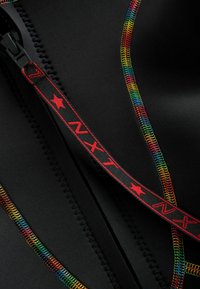 Une combinaison de plongée noire avec une couture colorée, dotée d'une fermeture éclair avec un tirette rouge et noire marquée "NXT" et d'un accent en forme d'étoile.
