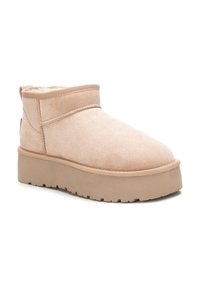 Botas de tobillos de ante beige con un interior suave, suela plana y plataforma, y un diseño minimalista que cuenta con sutiles detalles de costura.