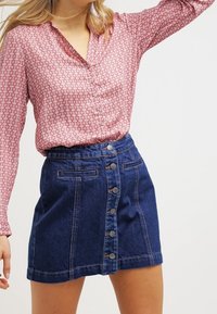 Blouse rouge à motifs avec un col, associée à une jupe en denim A-line bleu marine dotée de boutons avant et de deux poches latérales.