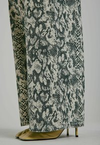 Pantaloni cu imprimeu de șarpe în nuanțe de bej și verde, cu o textură netedă și un design cu picioare largi, asortați cu tocuri ascuțite bej.