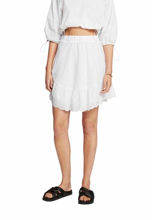 Jupe en coton blanc avec ourlet volants, dotée d'un bord festonné et de détails en œillets. Associée à des sandales noires à enfiler. Style décontracté, coupe ample.