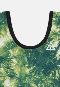 Zaļš bez piedurknēm tops ar palmu lapu rakstu, melnu apkakles apdari un balto logotipu apakšējā labajā pusē. Mīksta, teksturēta auduma.