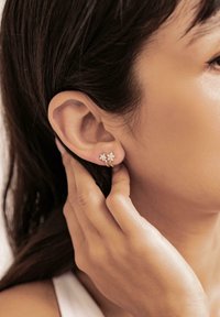 Silver star-shaped earrings with three small gemstones, worn on a model's earlobe, featuring a smooth surface and minimalistic design.