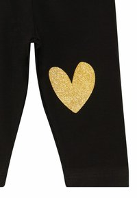 Sorte leggings med et stort glitrende guldhjerte-mønster på venstre side. Stoffet ser glat ud med en tætsiddende design.