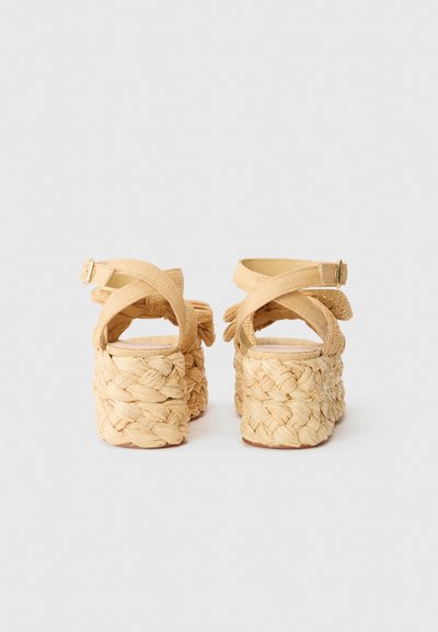 Tan platform sandals with a braided straw heel, crisscross straps, and an ankle buckle. Smooth upper material, open back design.