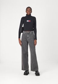 Maglione a collo alto nero a costine con logo ricamato, abbinato a jeans grigi a vita alta e gamba larga e scarpe chunky nere con zeppa.