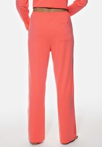 Korallfärgade loungebyxor med avslappnad passform, elastisk midja och en bakficka. Tyget verkar mjukt och lätt.