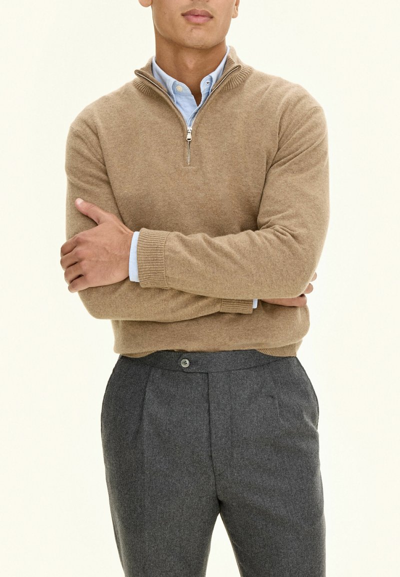 Lichtbruin zippered sweater gemaakt van zachte wol, gecombineerd met grijze goed zittende broek met knoopsluiting en voorsplitsingen.