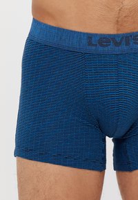 Modré boxerské šortky s vzorovaním a textúrovaným dizajnom, s modrým pásom so značkou "Levi's" a elastickým materiálom.