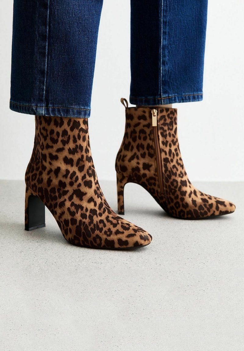 Bottines imprimé léopard à bouts pointus et talons carrés portées avec un jean court bleu foncé sur un sol gris.