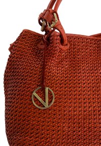 Rød vævet læderhandbag med en rund form, har et fremtrædende gyldent cirkulært mærke og glatte læderremme.