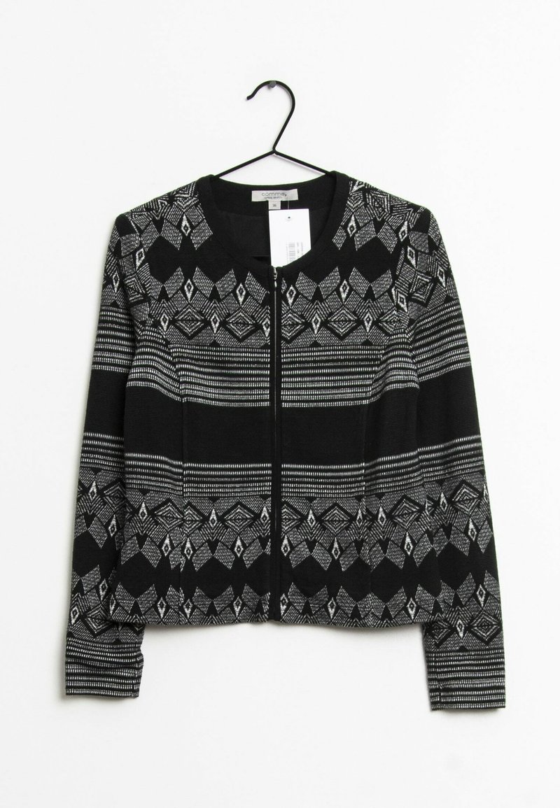 Pull zippé à motif géométrique noir et blanc avec manches longues, suspendu sur un cintre noir sur fond blanc.