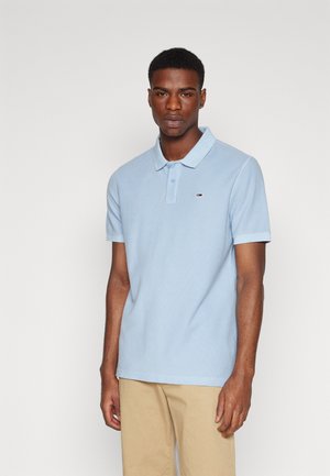 Polo de color azul claro confeccionado en tejido de algodón con un acabado texturizado, que cuenta con una tapeta de tres botones y un pequeño logotipo en el pecho.