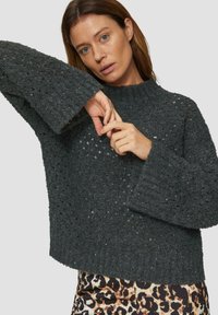Ciemnoszara sweter z dzianiny o luźnym kroju, złożonym wzorem i szerokimi rękawami. Teksturowana tkanina z delikatnym połyskiem. W połączeniu z wzorzystą spódnicą.