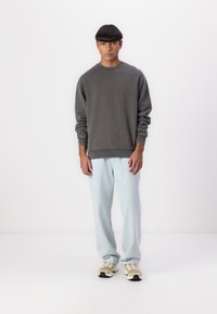 Šedý crewneck sweatshir s rebrovanými manžetami, kombinovaný s svetlomodrými rovnými džínsami a béžovými teniskami s sieťovinovými akcentmi.