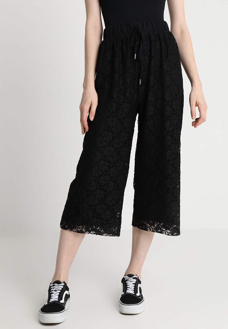 Čierne čipkované culottes s elastickým pásom, s jemným kvetinovým vzorom a skrátenou dĺžkou, v kombinácii s čiernymi teniskami.