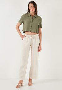 Olijfgroen cropped button-up shirt gecombineerd met beige linnen wijde broek. De outfit heeft een koordtaille en eenvoudige sandalen.