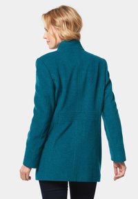 Tee-farbener Wollmischungs-Mantel mit aufstehendem Kragen, langen Ärmeln und taillierter Passform mit vertikalen Nähten und seitlichen Taschen.