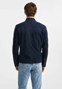 Navy skórzana kurtka z teksturowanym tyłem, dopasowanym fasonem, zamkami na mankietach oraz gładkim kołnierzem. Noszona z jasnoniebieskimi dżinsami.